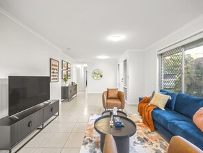 Ett modernt vardagsrum med en platt-TV, en soffa, ett soffbord och ett stort fönster.