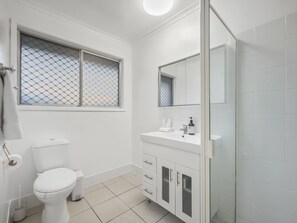 A bathroom with a toilet, a sink with a mirror, and a shower area. - Heart of Sunnybank | Prime Location | Great Value (Sunnybank)