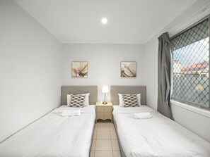 Une chambre d’hôtel avec deux lits simples, une table de chevet avec une lampe et des œuvres d’art accrochées aux murs.
