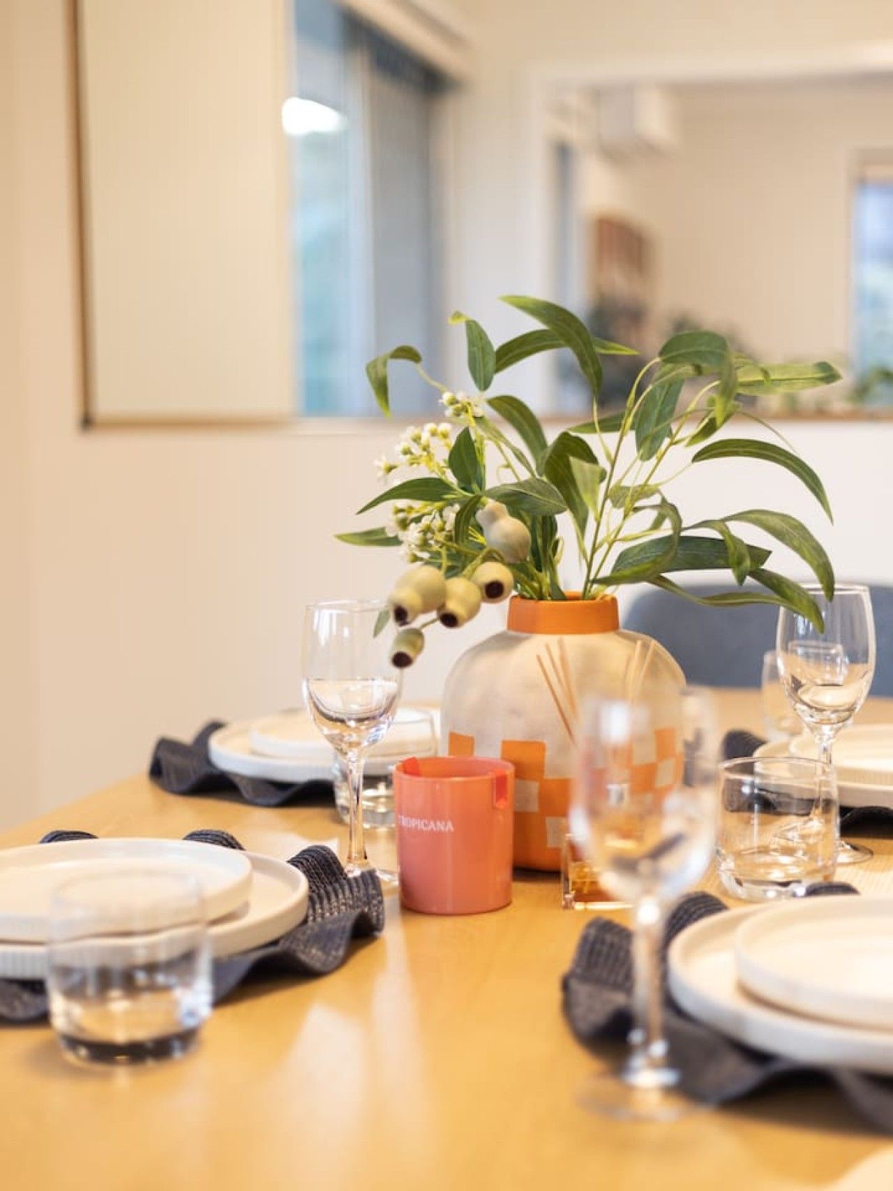 Una mesa de comedor dispuesta con platos, vasos y un jarrón con flores.