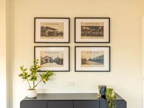 Un mur orné de quatre photographies historiques encadrées de Sunnybank, une prise de courant, une plante en pot et un petit objet décoratif posé sur un meuble de couleur sombre.