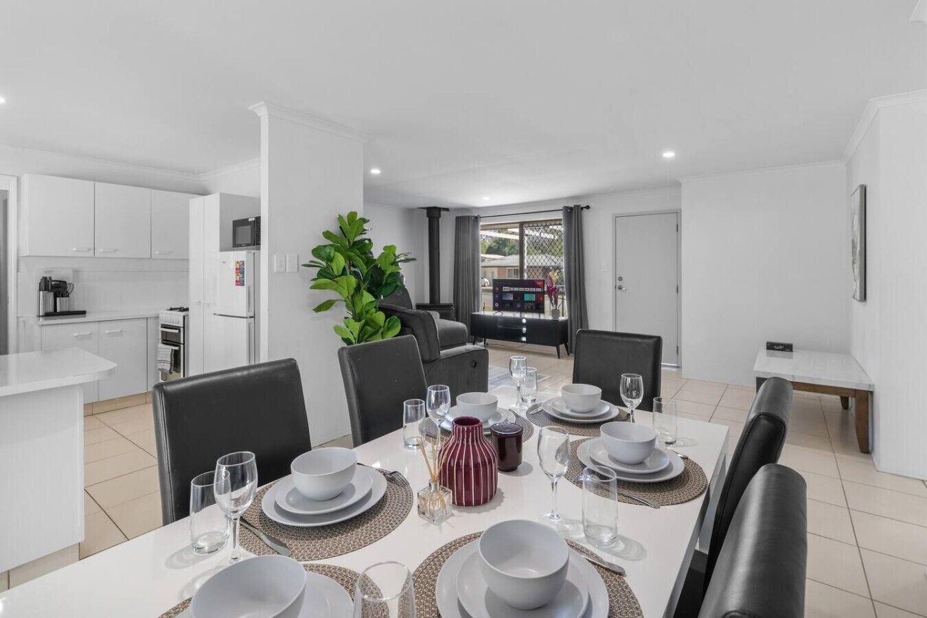 Un espace repas moderne avec une table blanche dressée pour six personnes, entourée de chaises noires.