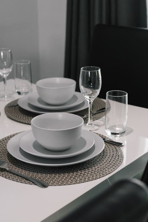 A dining table set with white bowls, plates, and glasses, with a fork and knife on the left.