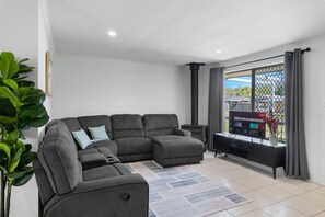 A modern living room with a sectional sofa, a flat-screen TV, and a large window with a view of the outside.