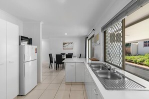 A modern kitchen with a refrigerator, a dining table with chairs, and a large window with a view of the outdoors.