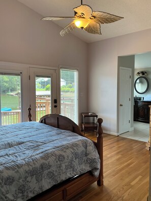 Un dormitorio con cama, ventilador de techo, puerta que da a un balcón y vistas al exterior.
