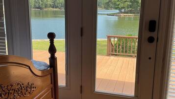 A bedroom with a wooden headboard, a wooden floor, and a view of a lake through a glass door.