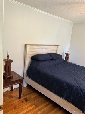 A single bed with a wooden headboard and dark bedding in a room with white walls and wooden flooring.