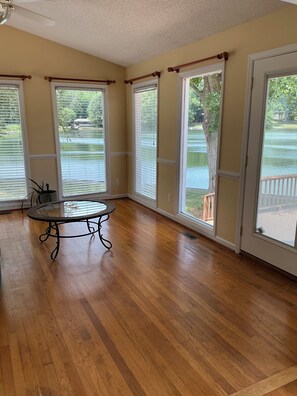 Una habitación con ventanas amplias, piso de madera y una mesa redonda.