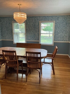 A dining room with a round table, wooden chairs, and a chandelier.