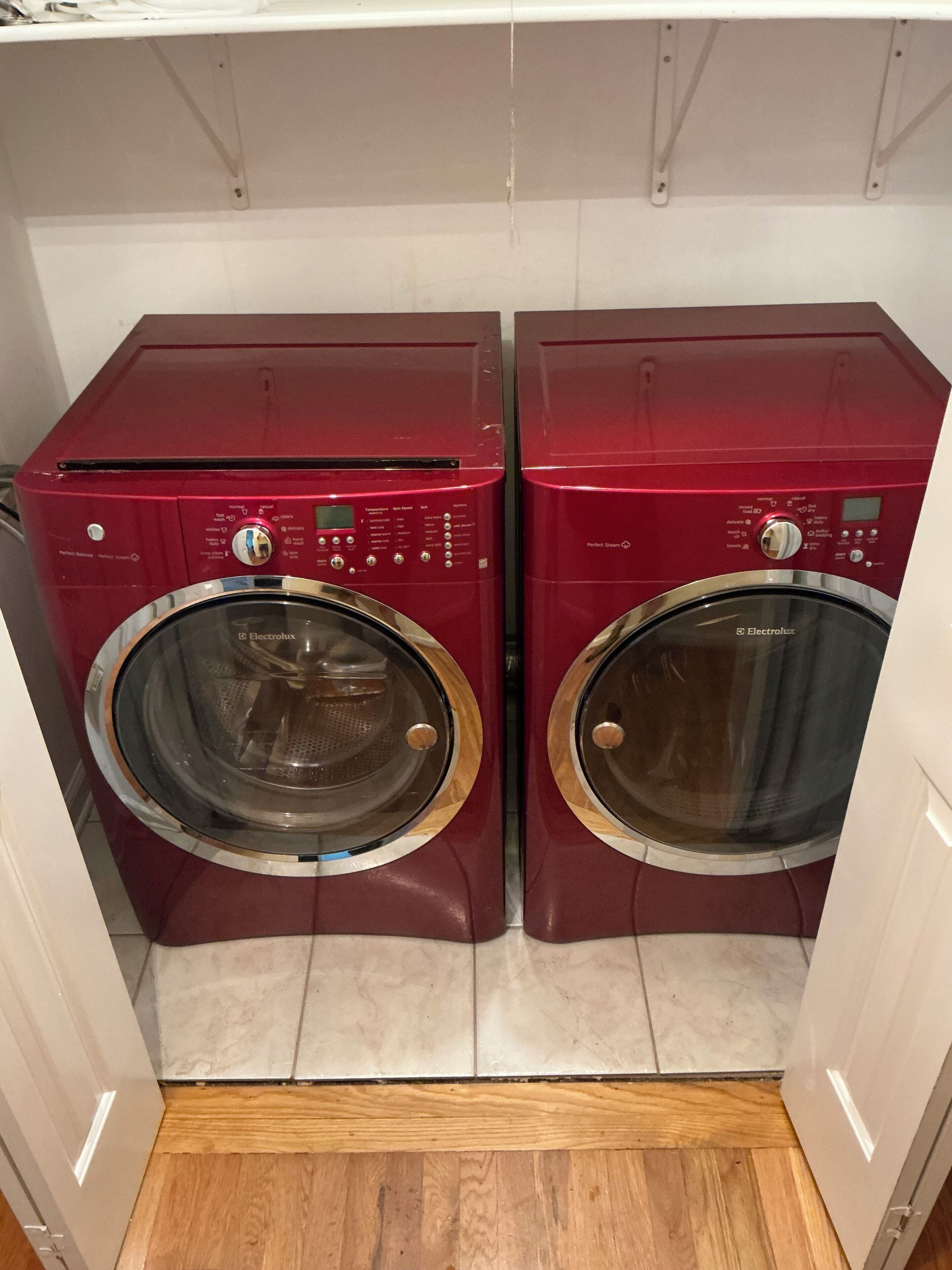 A pair of red front-loading washing machines in a laundry room with a wooden floor.