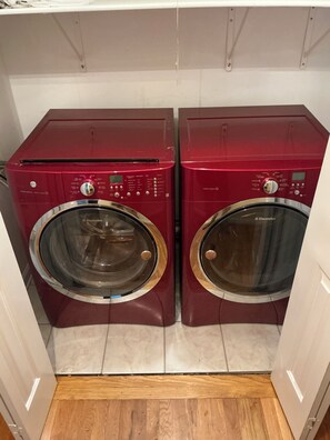 A pair of red front-loading washing machines in a laundry room with a wooden floor.