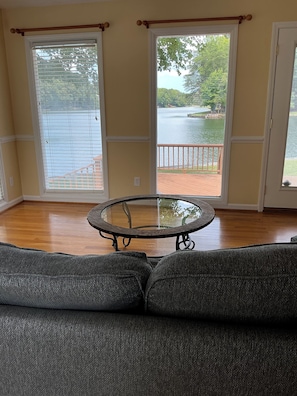 A room with a round glass table, a gray sofa, and large windows with a view of a lake and deck. - Simple Lake house in charming Summerfield with exceptional lake views! (Summerfield)
