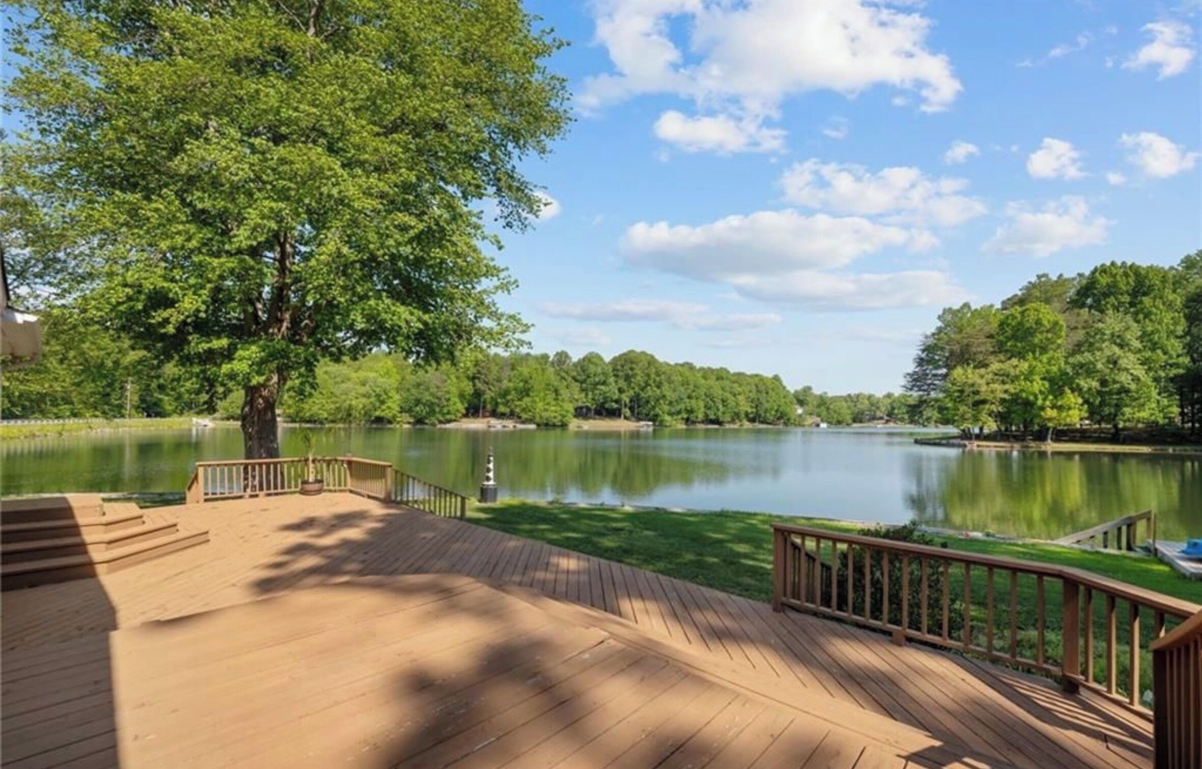 A wooden deck with a railing overlooking a calm lake surrounded by trees.
