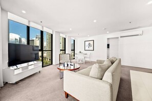 A modern living room with a flat-screen TV, a sofa, a coffee table, and a dining area. - Surfers Paradise Escape| carpark|Resort Facilities (Surfers Paradise)
