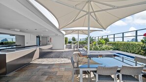 Et udendørs køkkenområde med bar, siddepladser og pool.