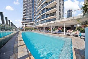 A swimming pool with lounge chairs and umbrellas, surrounded by modern buildings. - Surfers Paradise Escape| carpark|Resort Facilities (Surfers Paradise)