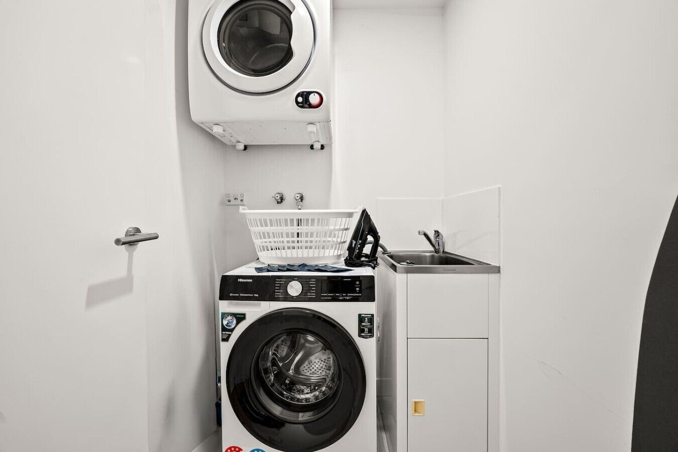 A compact laundry room with a front-loading washing machine, a dryer, and a small sink.