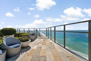 Ein Balkon mit Meerblick, Blumentöpfen und Korbmöbeln.