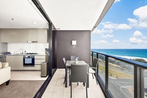 A modern kitchen with a built-in oven, a dining area with a table and chairs, and a balcony with a view of the ocean. - Surfers Paradise Escape| carpark|Resort Facilities (Surfers Paradise)
