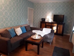 Een woonkamer met een bruine bank, een klein tafeltje en een televisie op een houten kast.