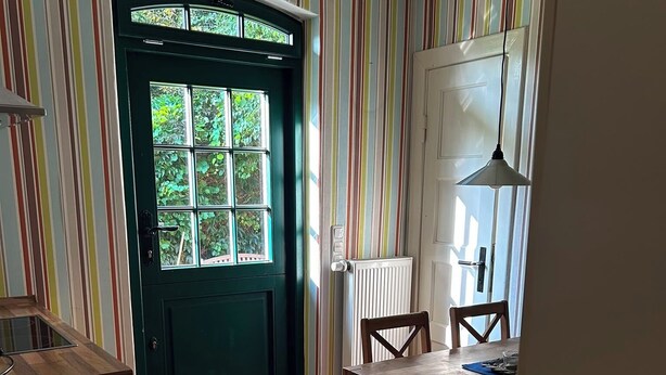 Uma cozinha com porta verde, mesa de jantar com cadeiras e janela com vista para o verde.