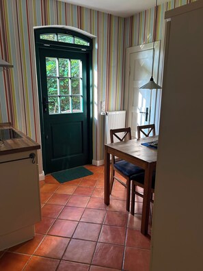 Eine Küche mit einer grünen Tür, einem Esstisch mit Stühlen und einem Fenster mit Blick ins Grüne.