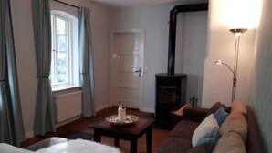 Uma sala de estar aconchegante com sofá, uma mesa com vela, lareira e janela com cortinas.
