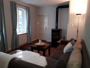 Ein gemütliches Wohnzimmer mit einer Couch, einem Tisch mit Kerze, einem Kamin und einem Fenster mit Vorhängen.