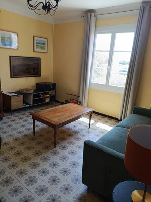 A living room with a sofa, a wooden table, a television, and a window with curtains. - A typical Provençal house, just a 10-minute walk from Almanarre Beach! (Hyères)