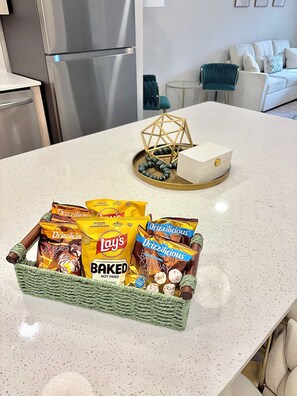 Un bancone della cucina con un cesto di snack che contiene patatine assortite e un oggetto decorativo.