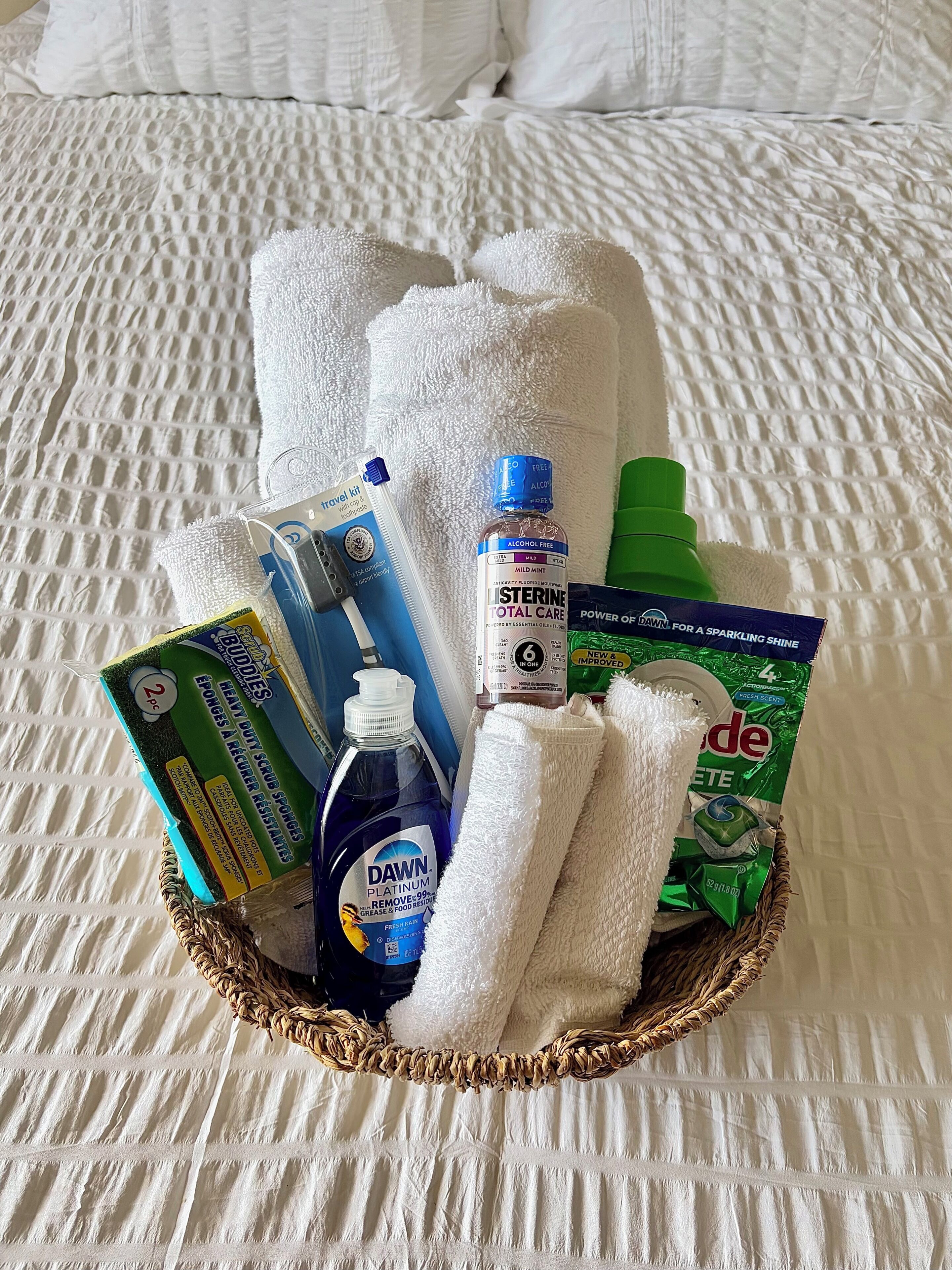 A basket containing toiletries on a bed with white bedding.