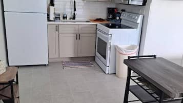 Une cuisine compacte équipée d’un réfrigérateur, d’un four à micro-ondes, d’une cuisinière et d’un évier. Un petit coin repas avec une table et des chaises est également disponible.