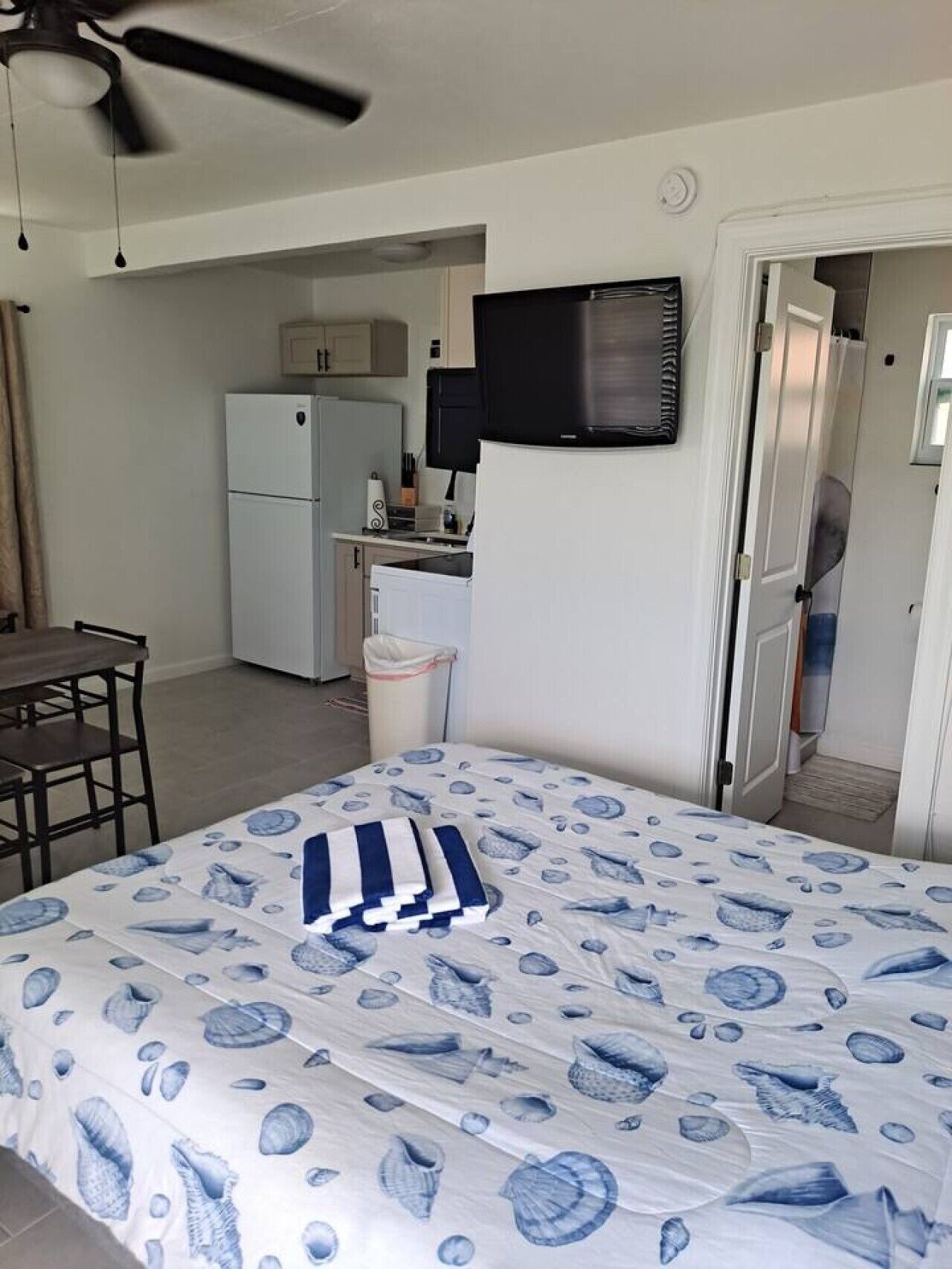 A hotel room with a bed, a desk, a chair, a television, a refrigerator, and a kitchen area.