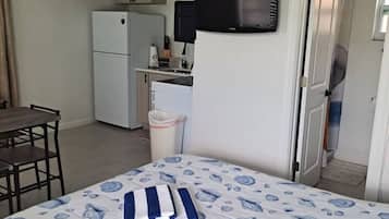 Une chambre d’hôtel équipée d’un lit, d’un bureau, d’une chaise, d’une télévision, d’un réfrigérateur et d’un coin cuisine.