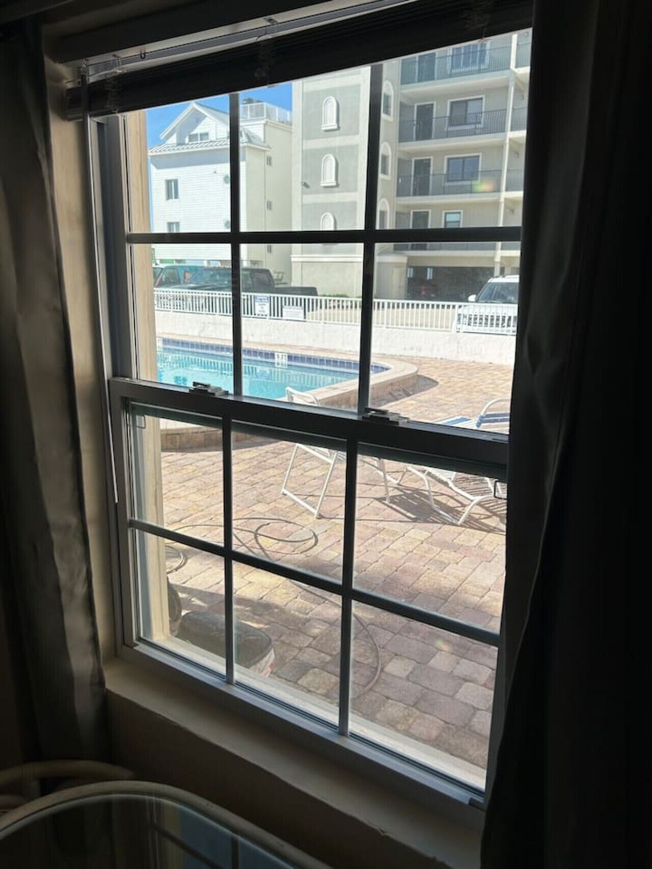 A window with a view of a swimming pool and a building with multiple balconies.