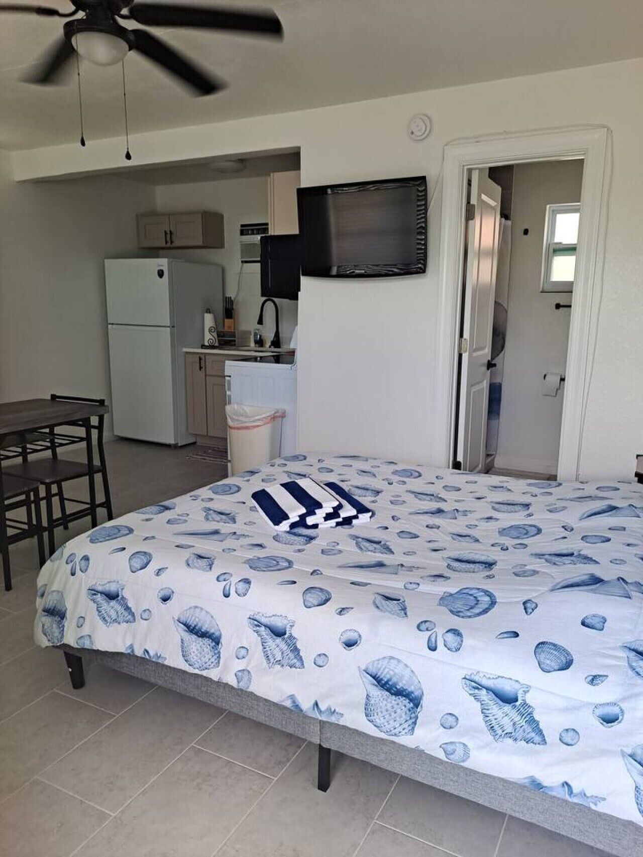 Ein Schlafzimmer mit Bett, Deckenventilator, einer Küchenzeile und einem Badezimmer.
