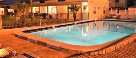 Ein Swimmingpool mit Backstein-Terrasse, Liegestühlen und einem eingezäunten Bereich.