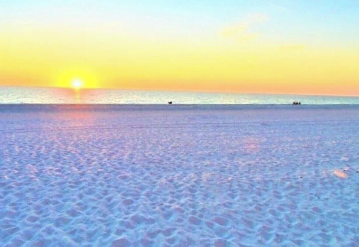 Una playa con atardecer, mar tranquilo y huellas en la arena.