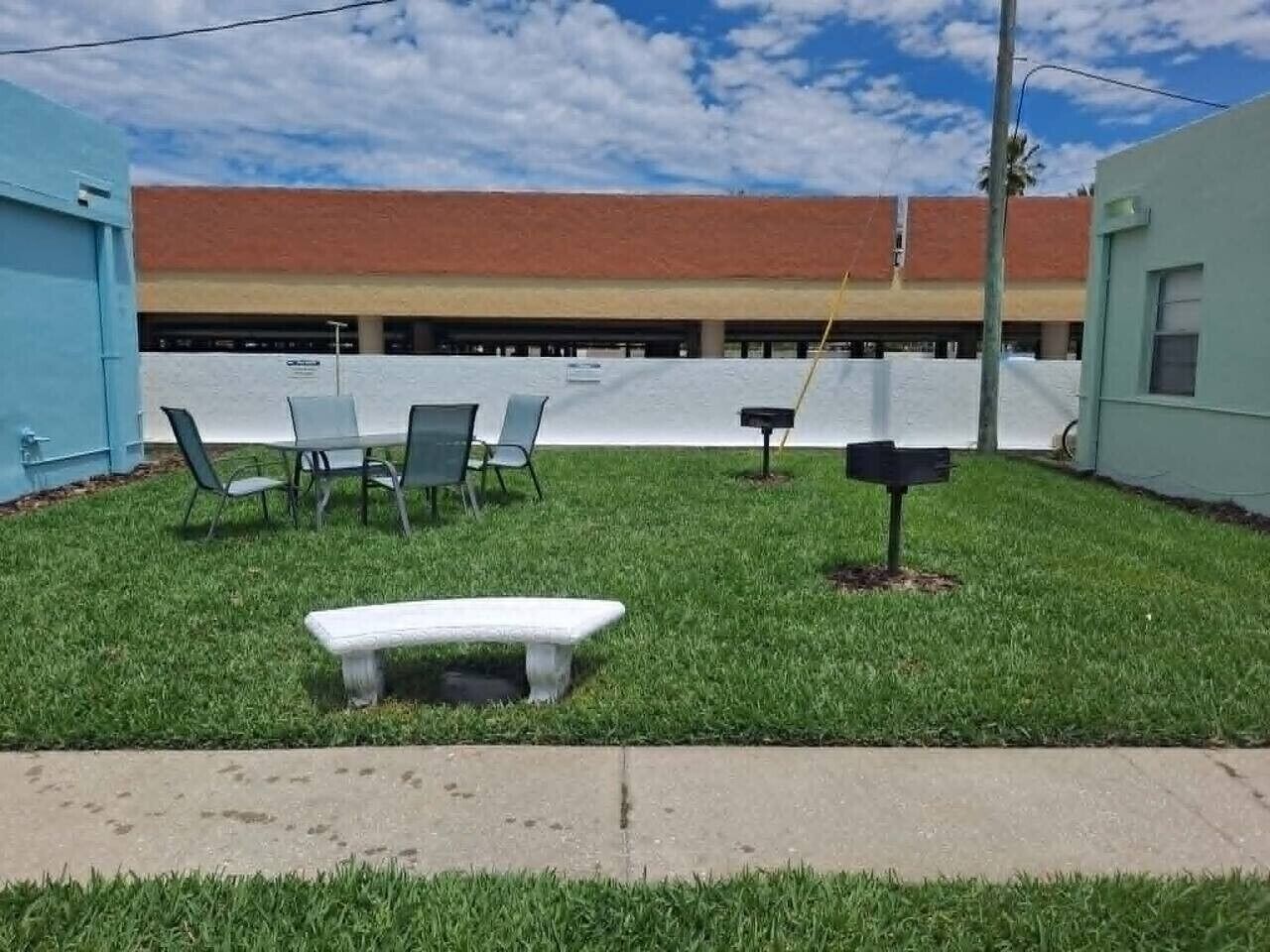A grassy outdoor area with a bench, chairs, and a mailbox.