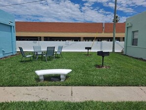 A grassy outdoor area with a bench, chairs, and a mailbox. - Poolside Studio-Steps to Beach! (Redington Shores)