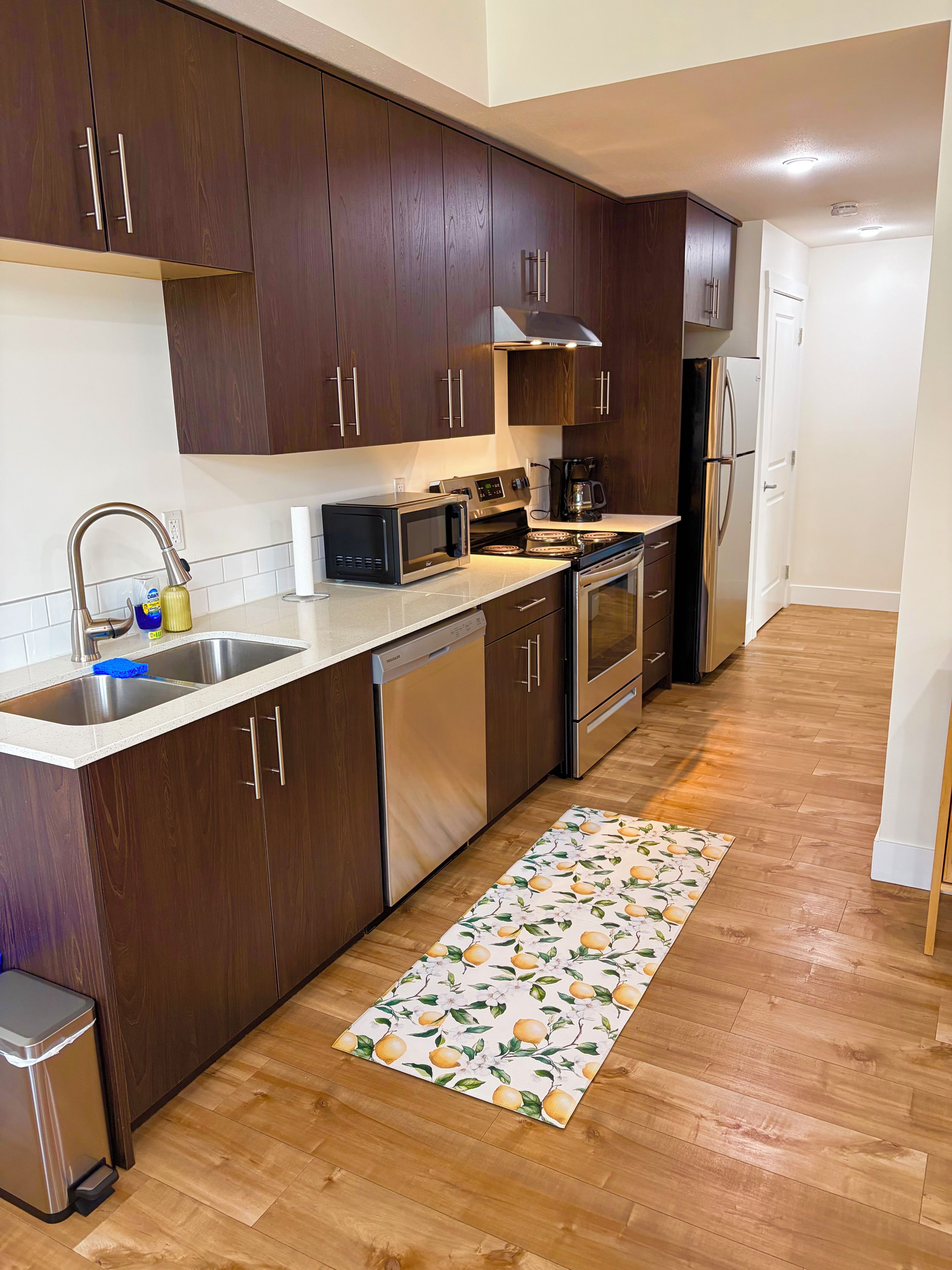 A modern kitchen with dark wood cabinets, stainless steel appliances, and a wooden floor.