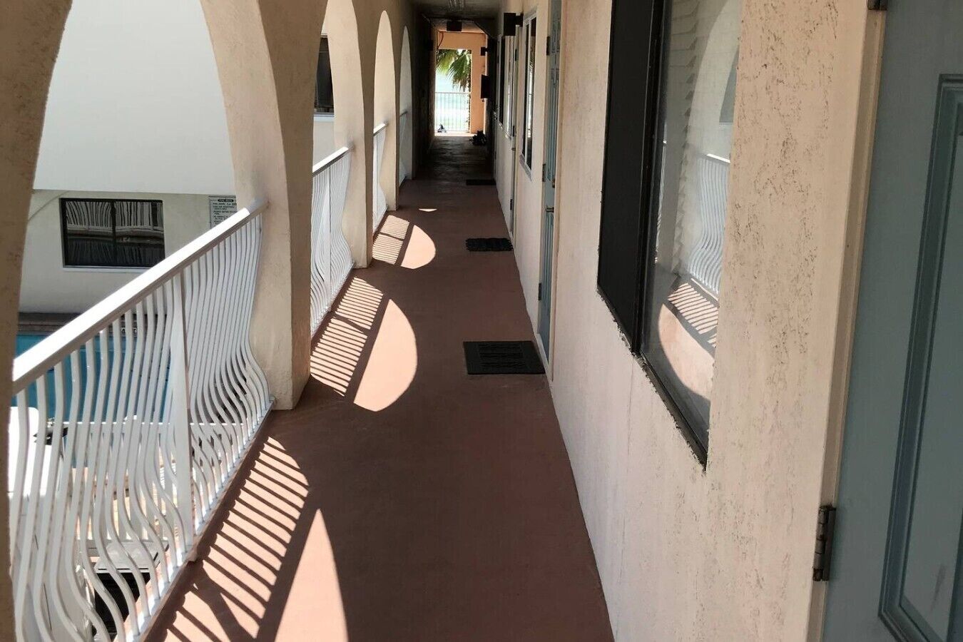A corridor with a series of arches and windows, leading to a door.