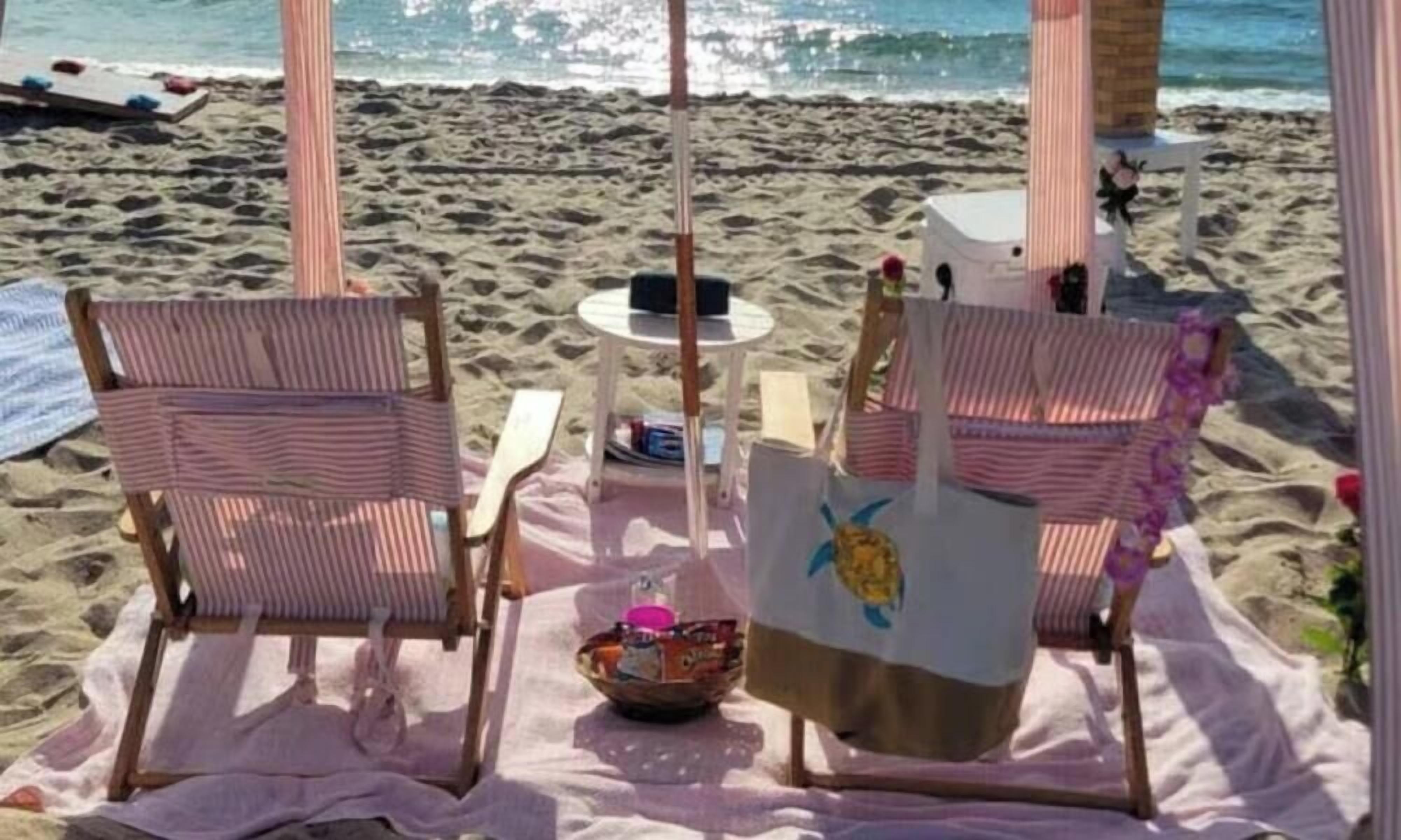 A beachside seating area with striped chairs, a table, and a sun umbrella.