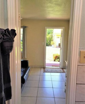 A hallway with a tiled floor leading to a door, a black sofa, and a towel rack. - Beachside Mini-Condo w/ Pool on Redington Beach! (Redington Shores)