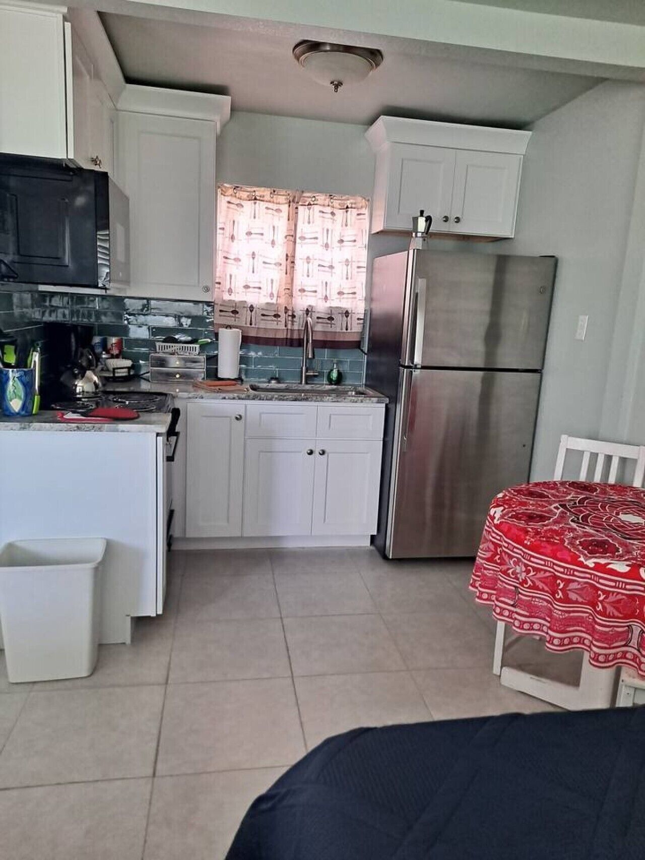 Una cocina compacta con armarios blancos, un refrigerador de acero inoxidable y un microondas.