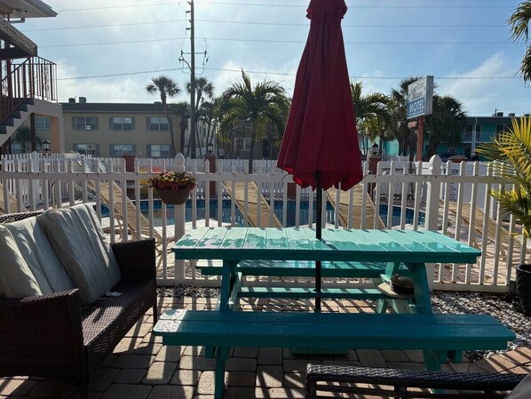A patio area with a picnic table and a red umbrella, surrounded by a white picket fence.
