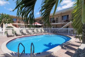 Ein Swimmingpool mit weißem Zaun, Liegestühlen und einem Gebäude mit Balkon im Hintergrund.