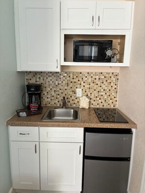 A compact kitchen with white cabinets, a stainless steel sink, a microwave, a coffee maker, and a dishwasher.