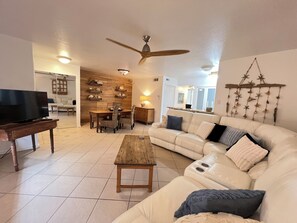 A living room with a television, a wooden coffee table, a white sofa, and a dining area with a wooden wall and shelves. - 3 min walk to BEACH! Great 2 Bed/2 Bath Condo! Well-equipped for FUN in the SUN! (Corpus Christi)